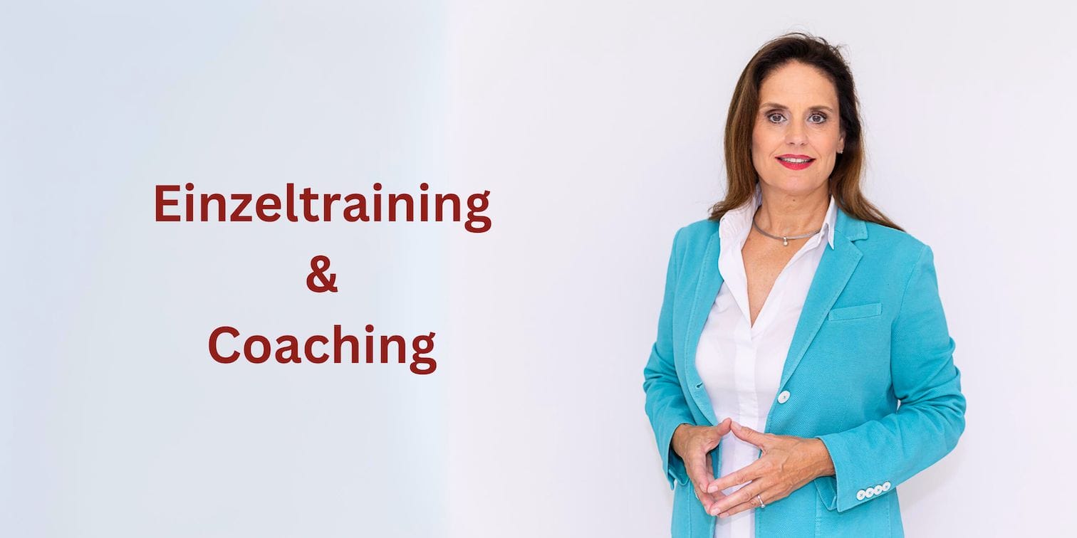 Eine Frau mit langen braunen Haaren, einem blauen Blazer und einem weißen Hemd steht vor einem weißen Hintergrund und blickt in die Kamera. Links von ihr steht in roten Buchstaben „Einzeltraining & Coaching“.